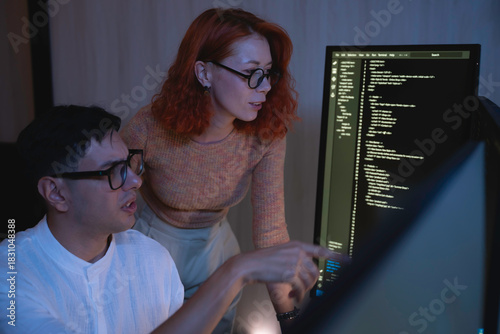 Two software developers collaborating at night, focusing on code review and debugging process on a computer screen, representing teamwork, innovation, and modern software development workflow.