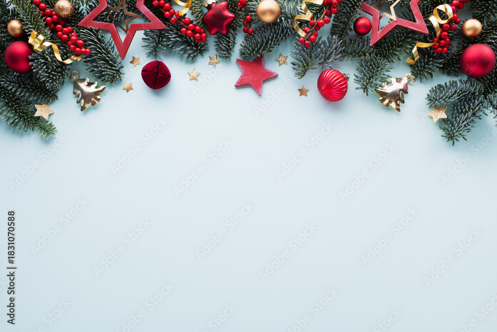 Obraz premium Festive winter frame with pine branches, red berries and shiny golden decorations on blue table top view. Christmas background in flat lay style.