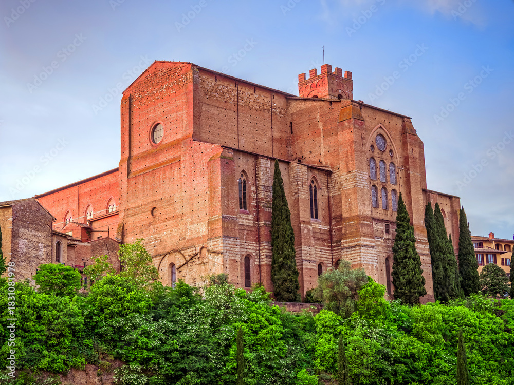 Obraz premium Basilica Cateriniana di San Domenico church rises above Siena, its imposing Gothic architecture framed from a low vantage point against the Tuscan sky. Travel in Italy.