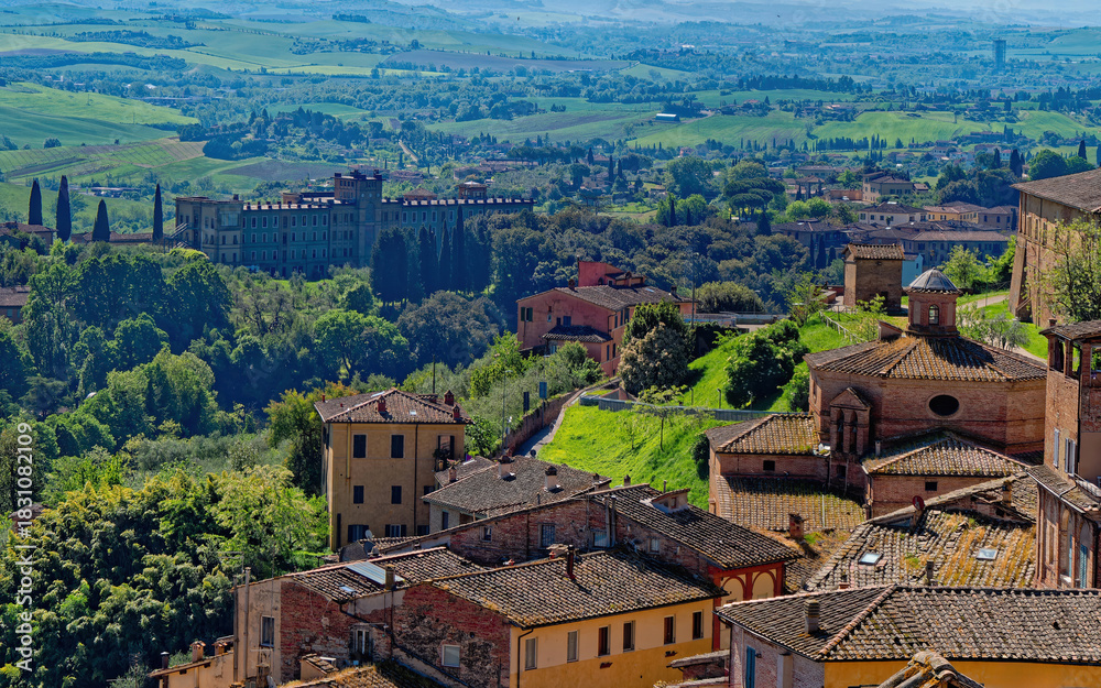 Obraz premium Aerial view of Siena’s rooftops and Villa il Pavone, where terracotta tiles, and Tuscan greenery blend into a timeless cityscape. Harmony between heritage and natural beauty from above.
