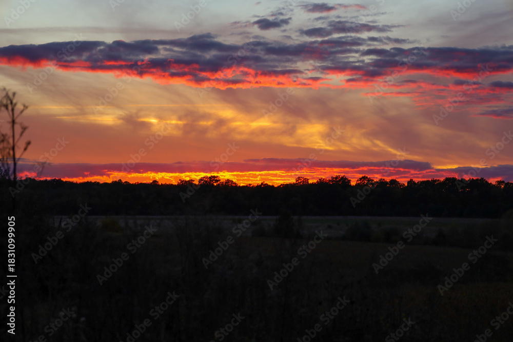 Obraz premium This is an enchanting sunset landscape, painting the sky with fiery hues of orange, red, and gold, featuring dramatic clouds that underscore the moment's majesty.