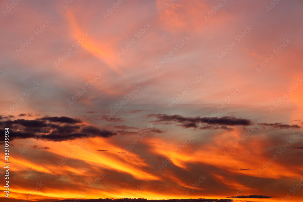Obraz premium A vibrant sunset paints the sky with dramatic shades of orange, red, and pink. Cirrus and stratus clouds are illuminated by the fiery light, creating a captivating and dynamic natural landscape.