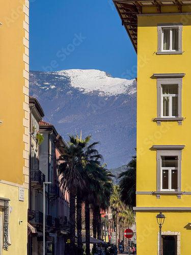 Mountain peak covered in snow seen between the buildings of a street, Riva del Garda, Italy