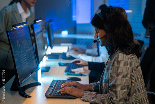 Indian customer service representative with headset typing on a keyboard while providing professional support late at night. Call center, IT support, telemarketing, online communication