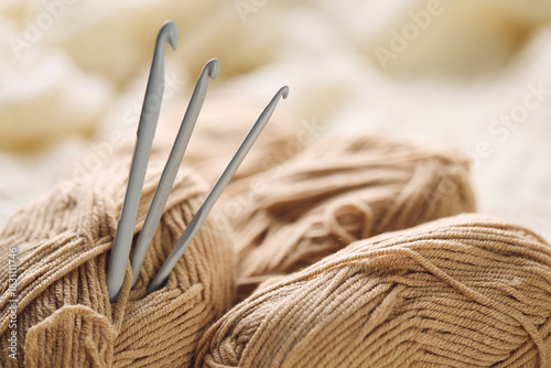 Crochet hooks and balls of beige and brown yarn on white knitted background. Knitting, crocheting supplies.