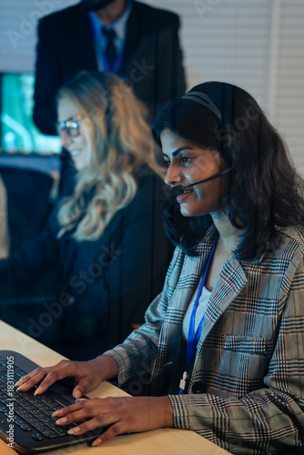 Indian customer service representative with headset typing on a keyboard while providing professional support late at night. Call center, IT support, telemarketing, online communication