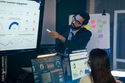 Executive is presenting customer engagement and NPS data on a large monitor in a dark office meeting. Business intelligence, corporate management, data analysis, project planning, and strategy session