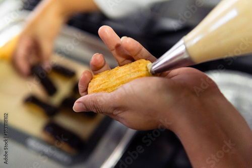 Chef hands piping cream into eclair pastry