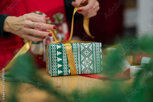 Hands tying gold ribbon on christmas present wrapping
