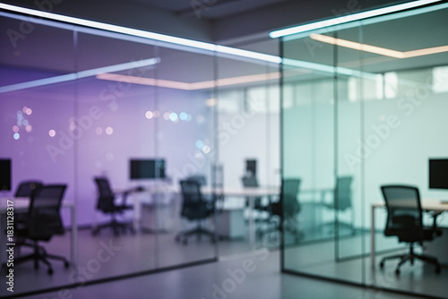 A modern office interior with glass partitions, desks, chairs, and computer monitors, featuring soft purple and blue lighting in a blurred, atmospheric shot.