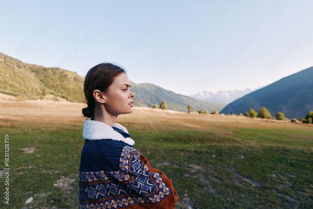 Naklejka premium Woman portrait in mountains and meadow, outdoors nature scene with thoughtful expression, standing in a landscape field wearing a patterned sweater, serene travel solitude mood.