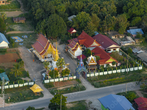 Aerial view of golden temples stand resplendent amidst lush greenery, their ornate roofs gleaming against the clear sky, Tambon Wichet Nakhon, Chang Wat Lampang, Thailand.