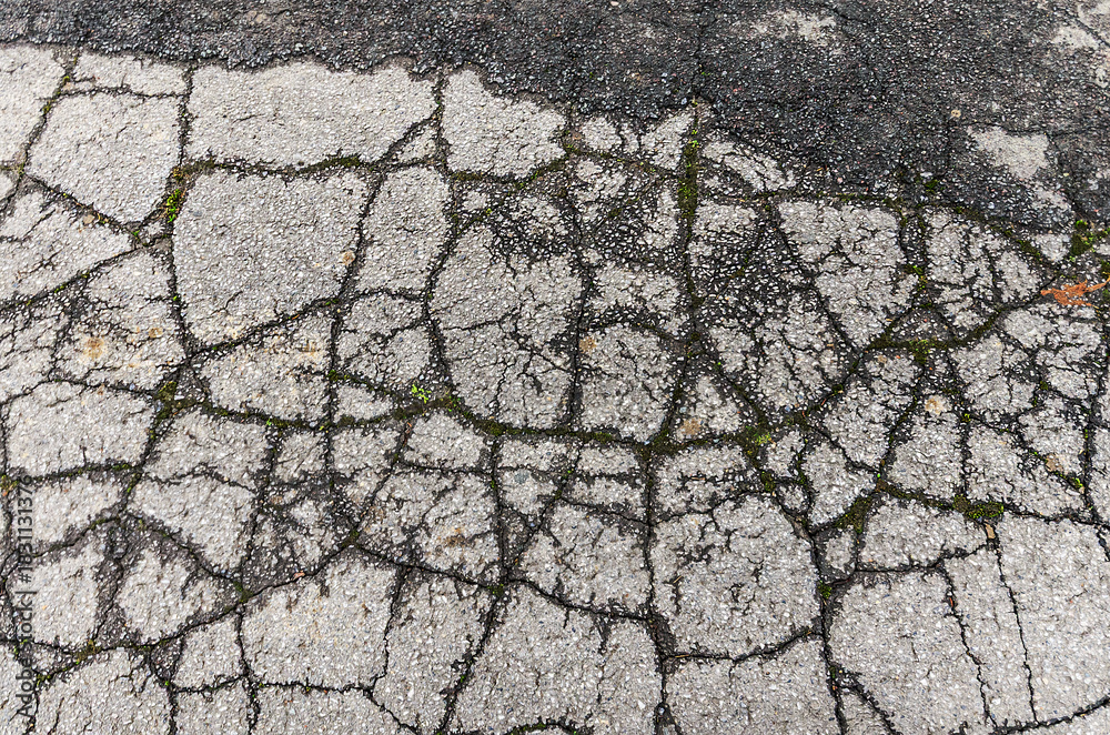 Obraz premium The cracked asphalt surface reveals a network of fissures and imperfections, highlighting the effects of time and wear