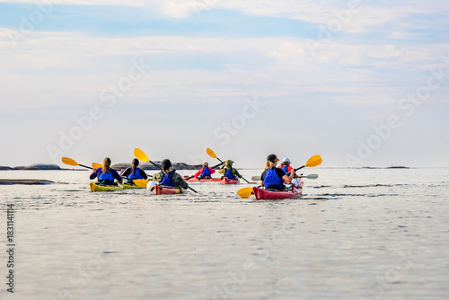 A group of people sea kayaking on the calm, clear waters of Georgian Bay, Ontario, Canada, passing by smooth granite rock formations under a bright sky. room for text