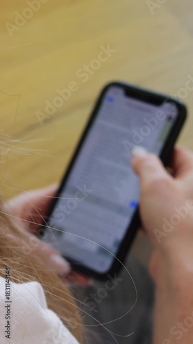 Woman scrolls social media on smartphone sitting at table in cafe. Female with long loose hair reads message in chat on mobile phone screen in coffee shop vertical video
