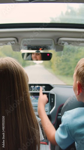 Family idyll concept where lovely happy brother and sister sitting at the rear seat of the auto,watch the way they are driving on and tell stories to their mom who's behind the wheel