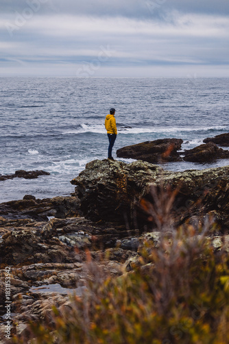 man standing on rocks looking at the ocean