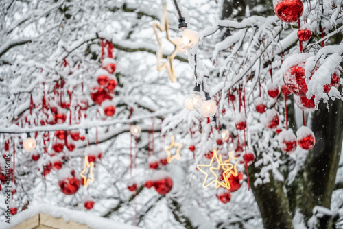 Red Christmas baubles and illuminated stars hang from wintery snow-covered branches above the Christmas market hut. Constance, Baden Württemberg, Germany.