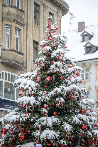 A pretty Christmas tree decorated with red baubles at the market place is covered in snow. Constance, Baden Württemberg, Germany.