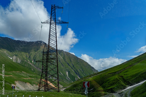 Electricity pylon above green mountain pass under bright blue sky