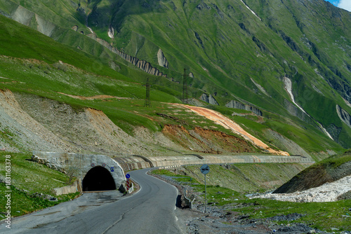 Narrow mountain road entering short tunnel beneath steep green slopes