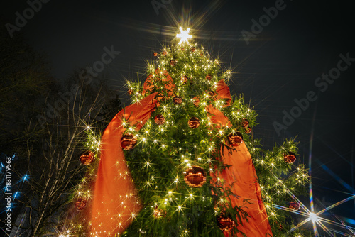 Christmas tree adorned with sparkling lights and red ornaments, featuring a large bow, creating a festive atmosphere during the holiday season with a star on top