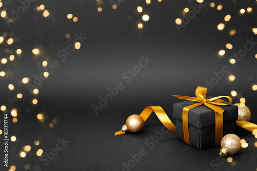 Black gift box with golden ribbon bow on black background