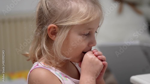 Little blonde girl enjoys a gummy vitamin at her kitchen table on a bright sunny day
