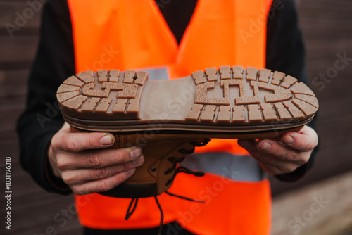 Принти на полотні Worker in a reflective safety vest holding a rugged work boot, close-up of the thick non-slip sole, showcasing durable industrial footwear for construction and heavy-duty environments
