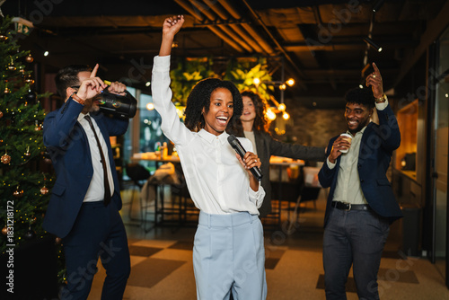 Diverse colleagues dancing and singing karaoke at office christmas party