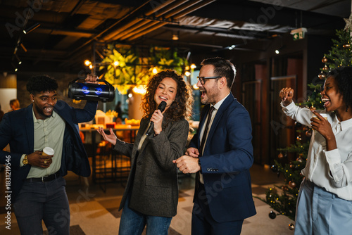 Diverse colleagues singing karaoke at office christmas party