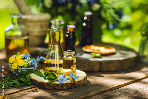 Mix of holistic flowers and herbs, salt, massage herb-infused essential oil in glass bottles. Aromatherapy, fragrance production. Herbal pure natural cosmetic ingredients on wooden background
