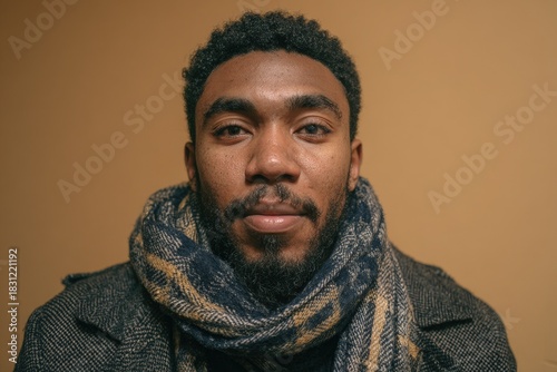 Portrait of a young man with dark curly hair wearing a patterned scarf and heavy coat against a plain background