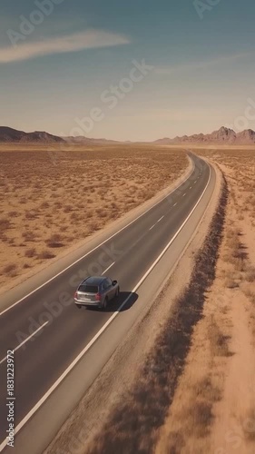 Aerial view of vehicle traveling on curved desert highway toward distant mountains