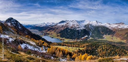Alpine Valley Golden Larches Snow Dusted Peaks Under Expansive Blue Sky, Winding Hiking Trail Through Colorful Meadow And Rocky Ridge, Crisp Autumn. Autumn panorama in Davos with a view of the lake.