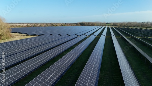 Aerial view of rows of solar panels stretching into the horizon, reflecting the clear sky above the green fields, Centenary Way, Spalding, England, United Kingdom.