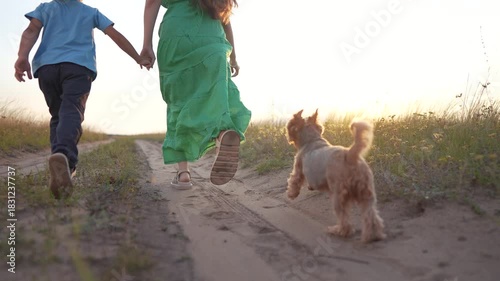 Woman and child walking down dirt road. Woman is walking dog outdoors with child. Family and friends in a field of nature at sunset. A girl and a woman strolling along a gravel lifestyle path.