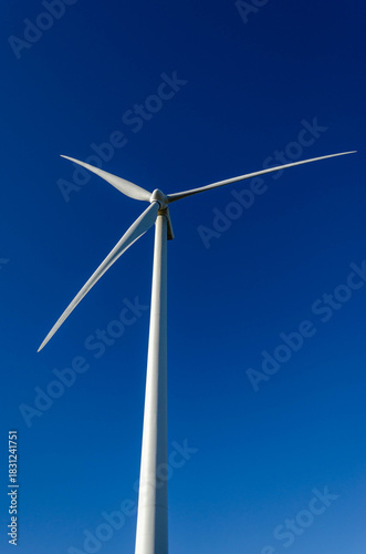 Wind turbine blades low angle view clean energy vertical blue sky.