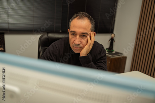 Man resting his head on hand while looking at a computer screen
