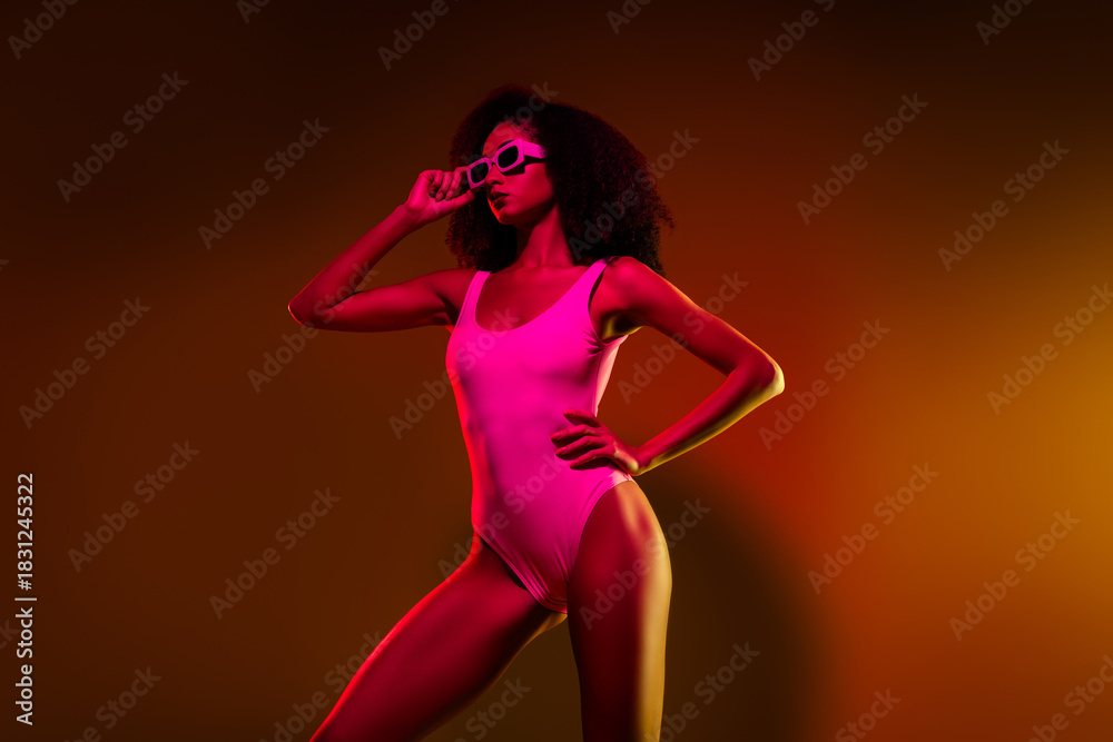 Fototapeta premium Glamorous Young Woman in Neon Bodysuit with Stylish Glasses and Vibrant Lighting in Modern Artistic Setting