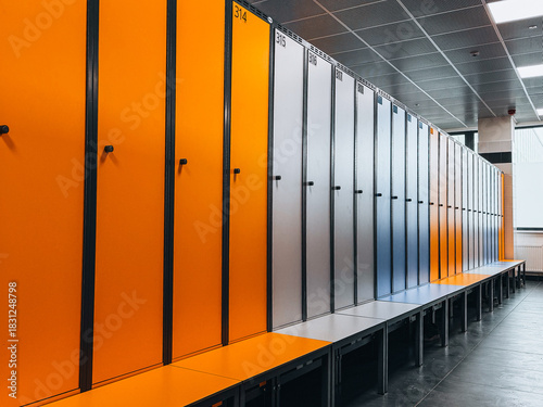 Row of vibrant orange and grey lockers in a modern gym changing room. Clean, organized interior with bold color contrast and minimalist design.