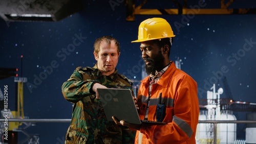 Fotografi Military officer in camouflage uniform uses walkie talkie on offshore platform, coordinating escort duty, crisis response and coastal defense to safeguard oil rig operations at sea
