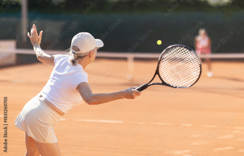 Fototapeta premium Rear view of focused european aged woman playing tennis match in open-air court of tennis club