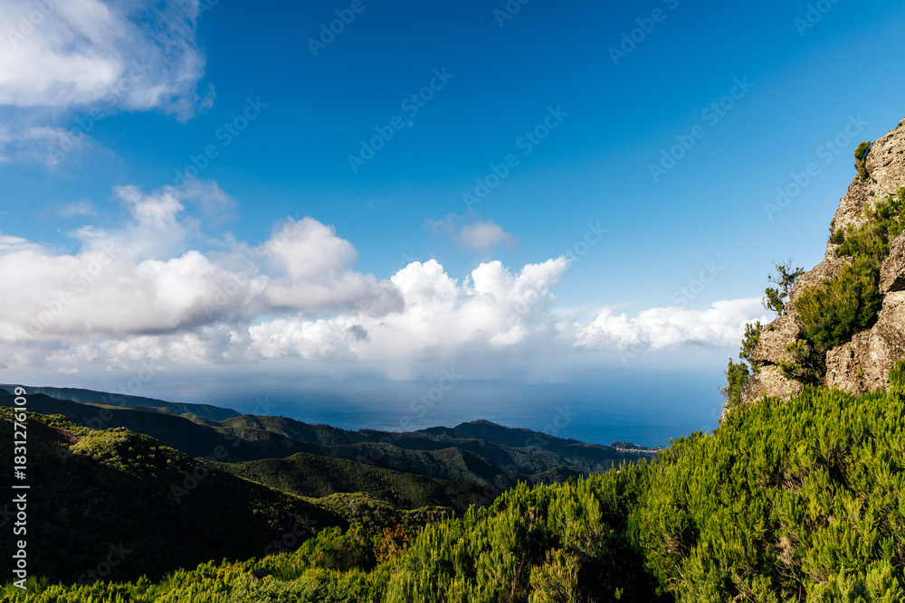 Naklejka premium Scenic mountain landscape with lush greenery and dramatic clouds under a bright blue sky, showcasing the beauty of nature and the tranquility of outdoor exploration