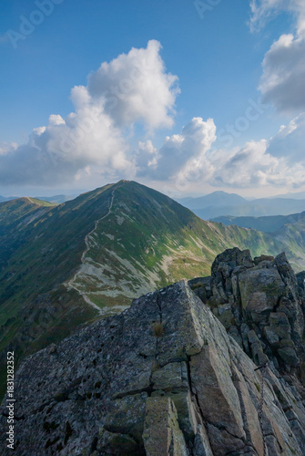 View of jagged rocks meet the sky, leading to a verdant peak under a sky dotted with fluffy clouds, a scenic vista of nature's raw beauty, Zuberec, Zilinsky kraj, Slovakia.