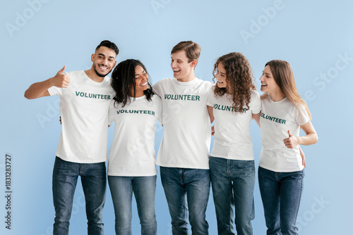 Obraz na plátně Five young adults stand closely together, wearing matching shirts that say Volunteer