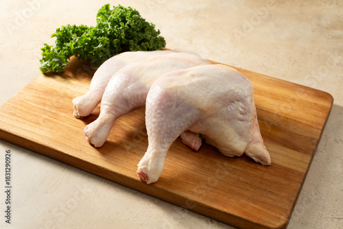 A view of several raw chicken quarters, on a wood board.