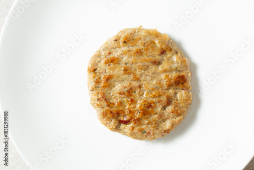 A top down view of a single chicken sausage patty, on a plate.