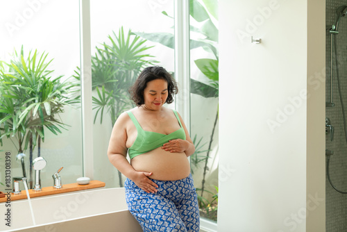 A pregnant woman gently cradling her baby bump in the bathroom