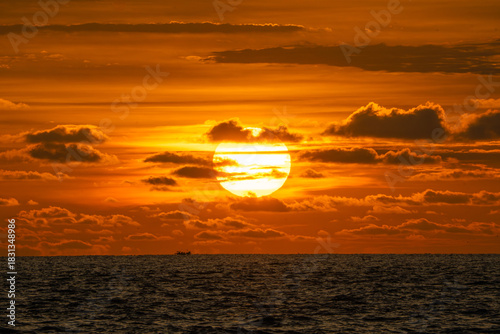 Golden Ocean Sunset with Dramatic Clouds. big Sun over the sea during a sunset with the sky coloured orange.